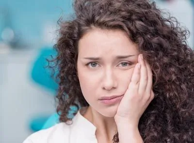 woman holding her mouth due to tooth pain prior to seeing the emergency dentists at Prosthodontic Associates of New Jersey